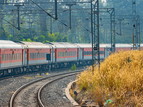 A view of a lengthy train travelling on the track with another empty track on the right hand side and trees on the left hand side, the distance from Pune to Goa is about 470 km on road.