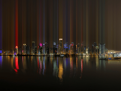 Skyline at night with illuminated skyscrapers reflecting on calm waterfront.