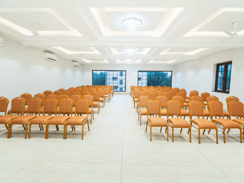 A banquet hall with orange chairs arranged in a theatre style seating arrangement - MGM Whispering Meadows