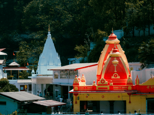 A close up shot of the vibrant red and yellow dome of Kainchi Dham surrounded by white buildings and lush green trees.