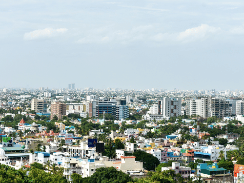 Panoramic view of a sprawling city centre with modern high-rise buildings and green trees under a bright, clear sky.