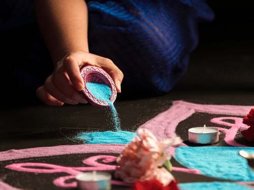 A person creating a kolam design on the floor using coloured powder and hand movements.