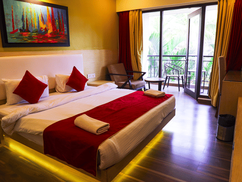 A bright hotel room with a yellow accent wall and a queen bed dressed with white and red linens and towel art.