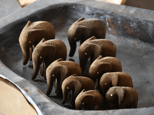 Hand-carved wooden elephant souvenirs displayed on a clay plate.