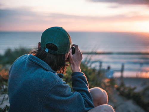 A photographer capturing the sunset by the sea during golden hour.