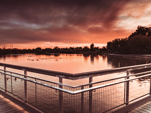 A view of a lake after a sunset with different hues in the sky, with trees in the distance.