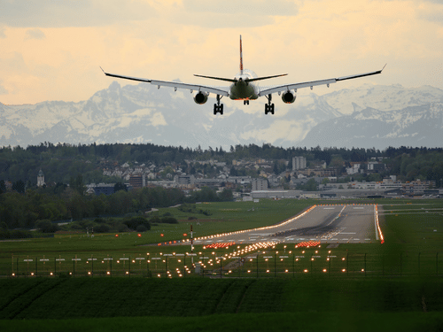 An aeroplane landing on the runway with greenery surrounding it .
