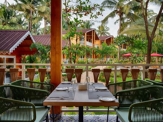 An image of the dining area with four chairs and a table in between and cabins in the background - Aralea Beach Resort by Stone Wood, Morjim