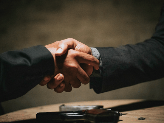A close-up of two people in dark suits shaking hands over a table | HHI Varanasi