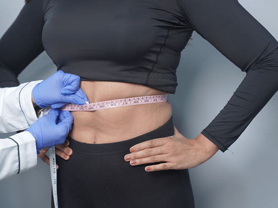 A person in activewear having their waist measured with a tape measure by someone wearing medical gloves.