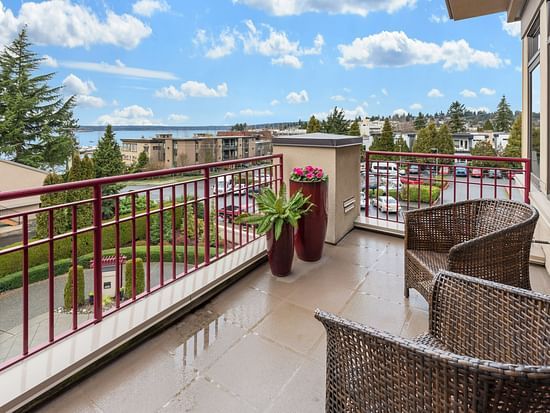a balcony in a house with two chairs and white clouds on blue sky in the background