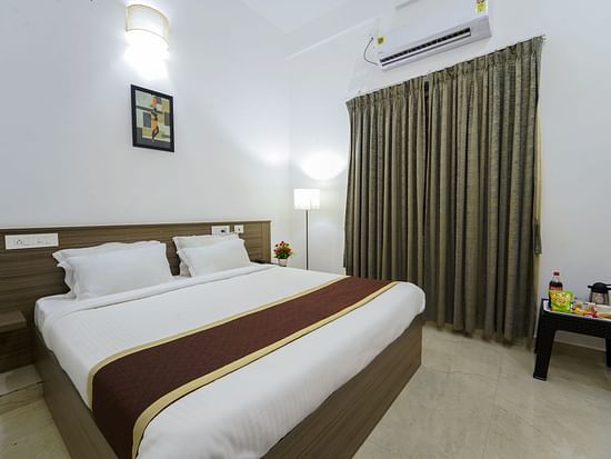 A double bed with side lamps, curtains on the window and an AC inside Deluxe Seaview Double Room - Le Poshe Beachview Pondicherry
