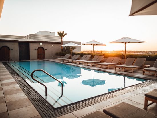 A swimming pool with loungers next to it and the sun setting in the background