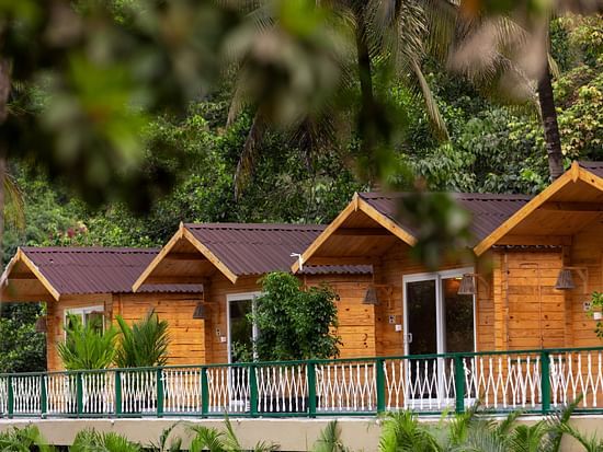 Row of cottages with a railing in front of them and nature in the background - Stone Wood Jungle Resort, Dandeli