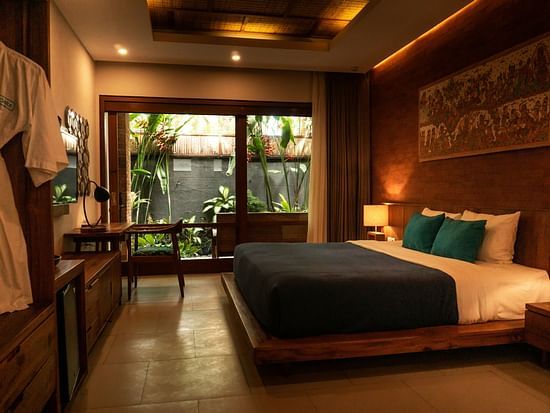 Warmly lit modern bedroom with wooden decor, king-sized bed, and garden view through large glass doors.