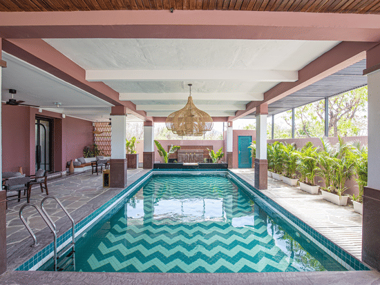 Indoor swimming pool at The Sierra Udaipur surrounded by plants on one side and seating area on the other side.. 