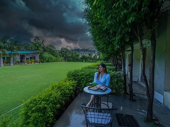 A side view of the garden area at Tattwaa, where a woman is seated, savoring tea and the beauty of nature.
