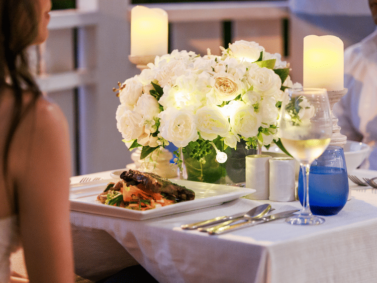 A table set with white flowers, candles, plated food, and wine at The Soco House, with two diners partially visible.