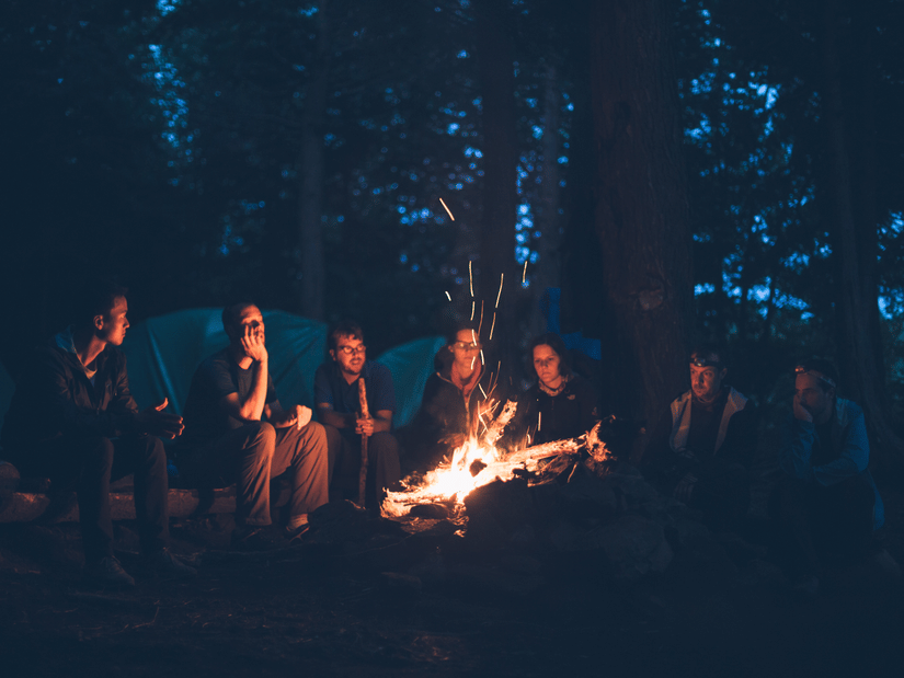 A group of people gathered around a campfire in a forest.