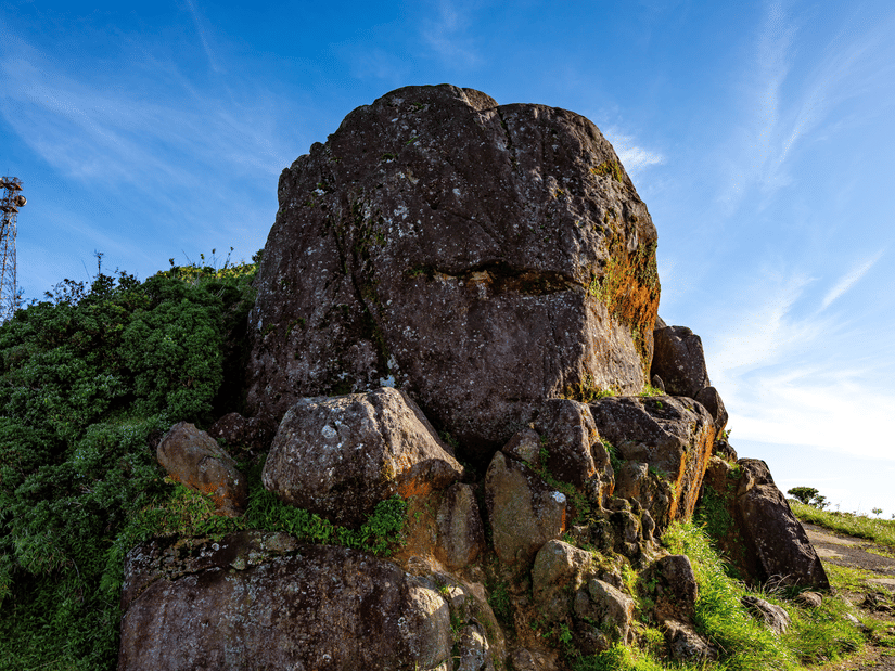 A striking natural rock formation rising above lush greenery under a clear blue sky, offering spectacular views of the surrounding landscape.