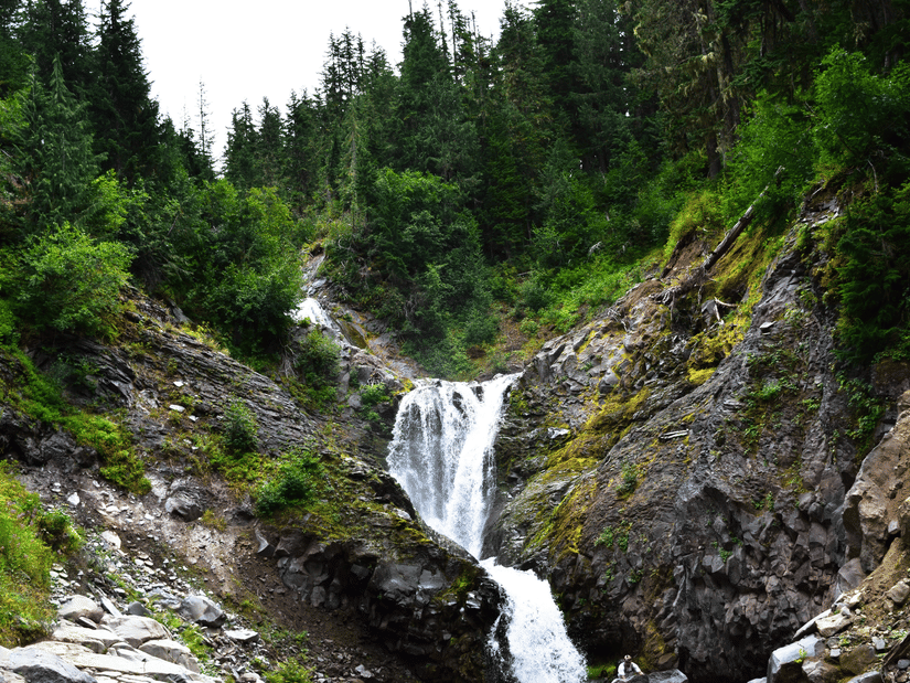 An overview of the waterfalls inside a forest with trees in the background, as seen during the day.