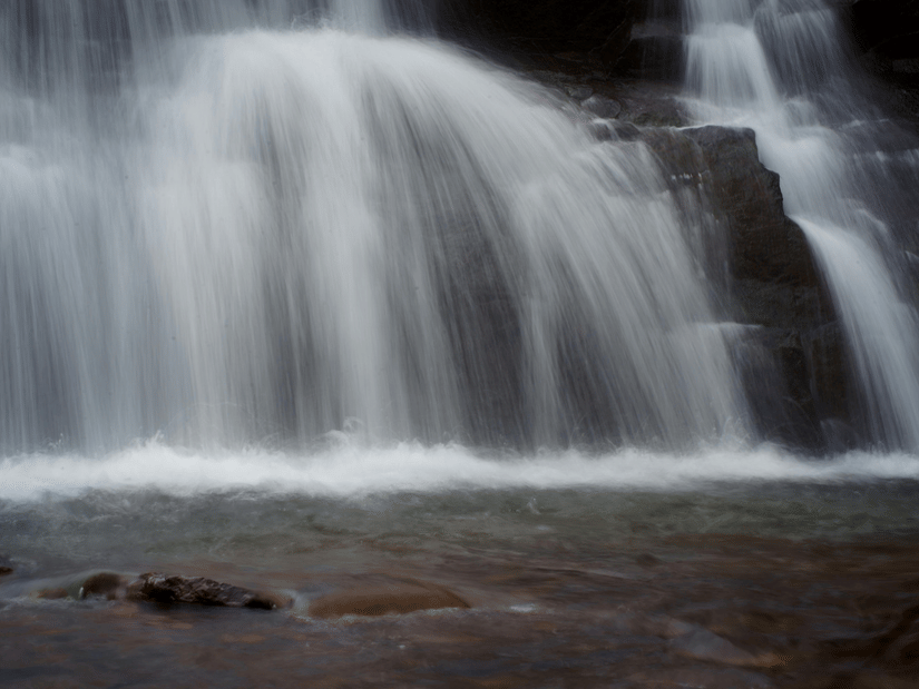 A smooth-flowing waterfall captured in motion, with water tumbling over dark rocks into a shallow pool.