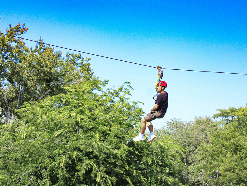 Person enjoying a thrilling zipline adventure above lush green forest, surrounded by trees beneath a bright blue daytime sky