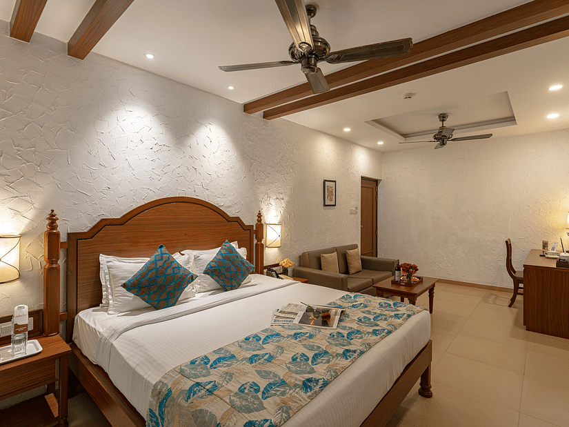 A hotel room featuring a neatly made and decorated bed, two wall-mounted lamps, a sofa, a side drawer, and a vanity.