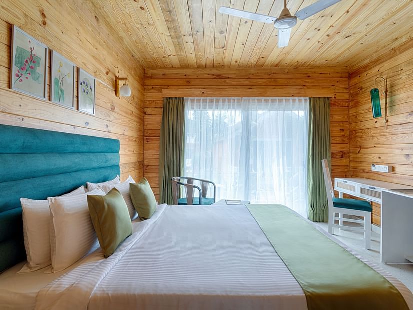 A warm, inviting bedroom featuring a large bed with a teal headboard and sage green accents, flanked by wooden walls and a sheer curtained window Aralea Beach Resort by Stone Wood, Morjim