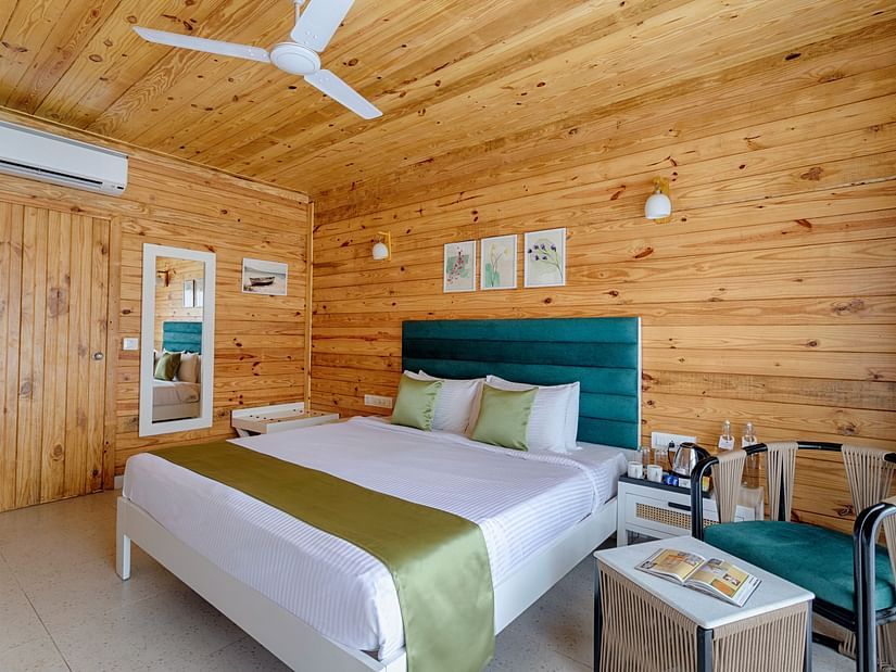 A bedroom with a white ceiling fan, AC unit, wooden walls, a teal headboard, and white bedding with a green accent Aralea Beach Resort by Stone Wood, Morjim