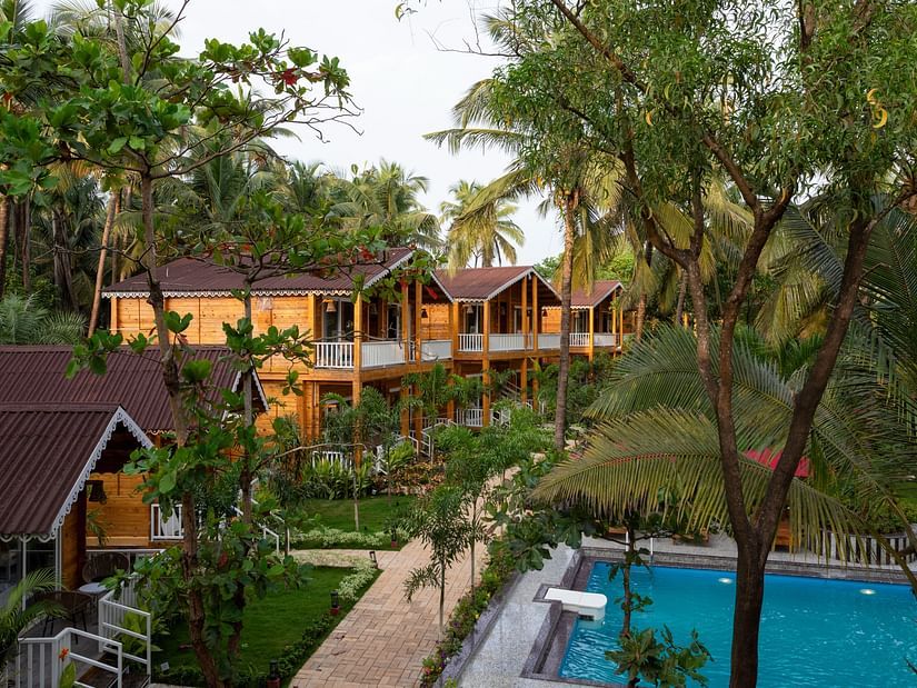 An elevated view of wooden resort cabins amidst lush greenery with a view of the pool and garden pathway - Aralea Beach Resort by Stone Wood, Morjim