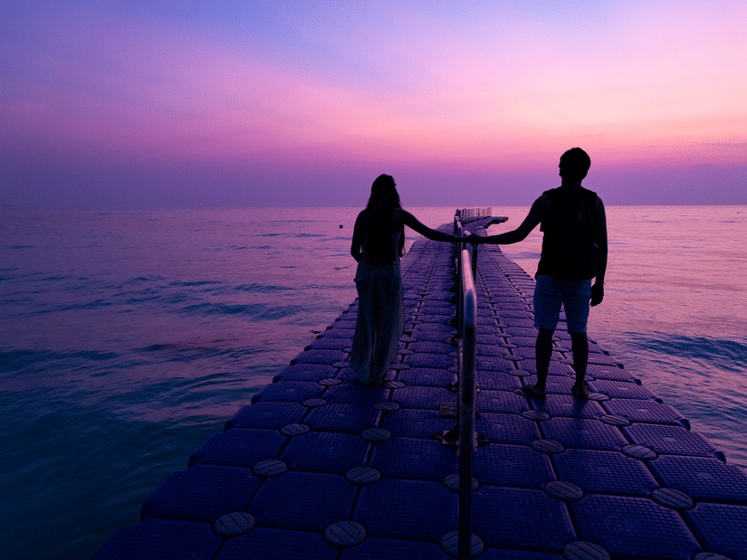 A couple walking during sunrise at Kalapathar Beach while standing on a man-made pier and looking at the sky