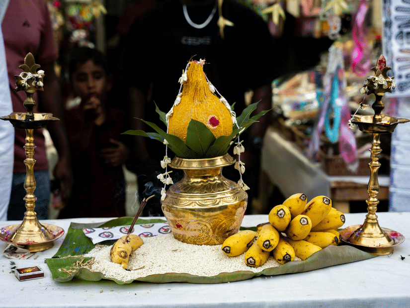 A traditional Hindu prayer setup with a brass Kalash, yellow bananas, and oil lamps on a white-covered table.