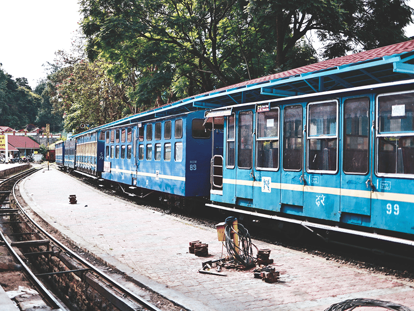 The blue Ooty Toy Train stands along a curved railway track amid the scenic Nilgiri landscape.