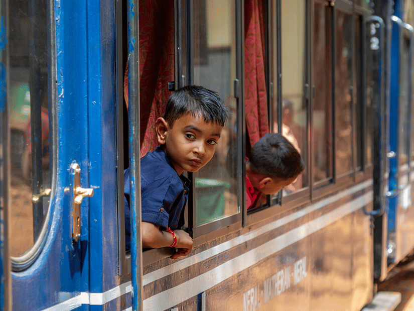 A close up view of the outer park of a blue train with kids looking out the window. There is no direct Coimbatore to Ooty train, the closest option is to arrive at Mettupalayam from Coimbatore and then taking another train to Ooty.