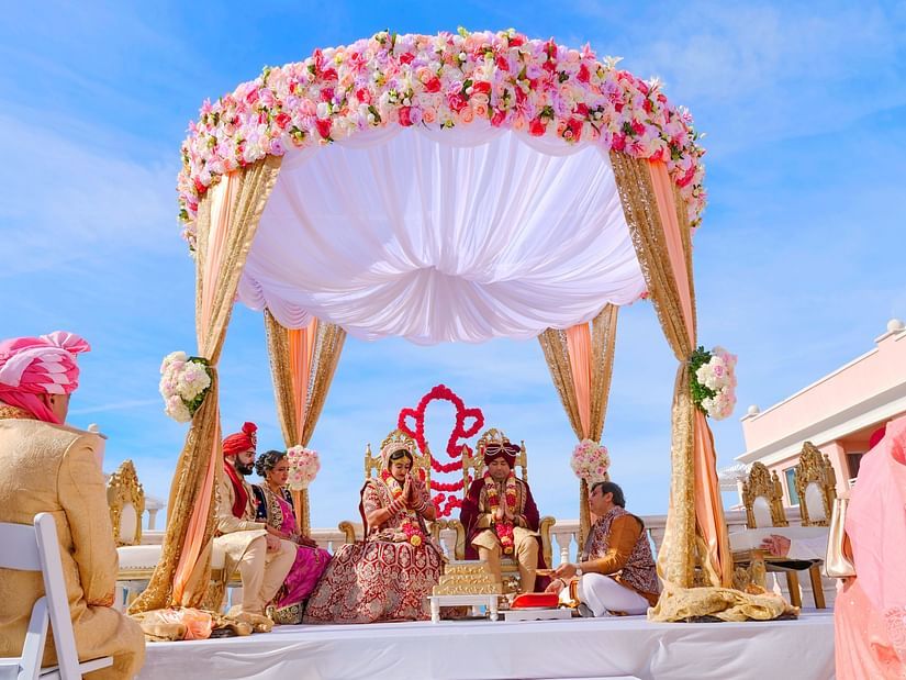 A wedding being performed in an open air setting with the bride and groom inside a canopy