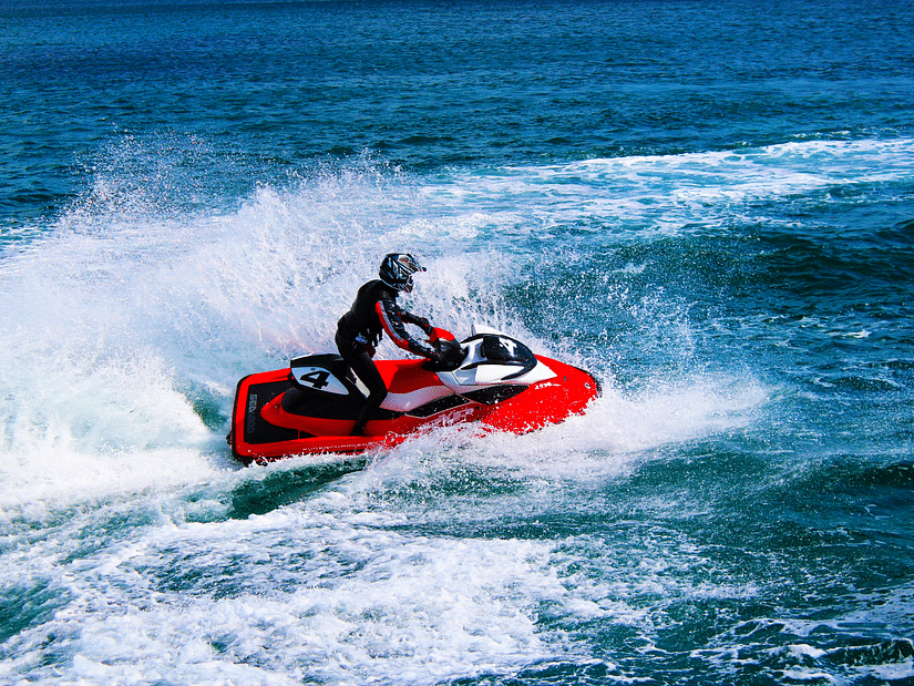 A person in full swimming gear riding a red jet ski in open waters with waves in view.