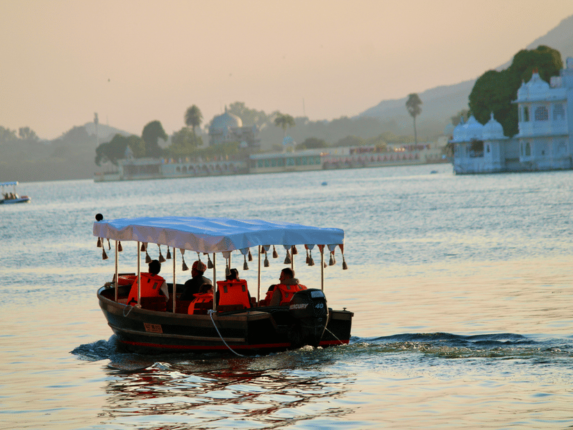 Tourist boat moving across Lake Pichola during sunset seen from the Gangaur Ghat.
