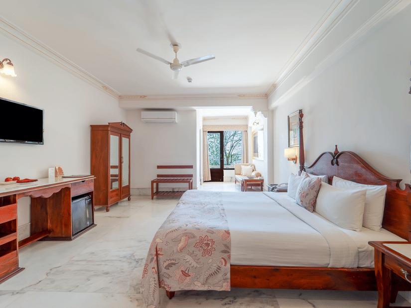 A wide view of a grand suite featuring a king size bed, dark wood furniture, and a wall-mounted television - Fateh Garh, Udaipur