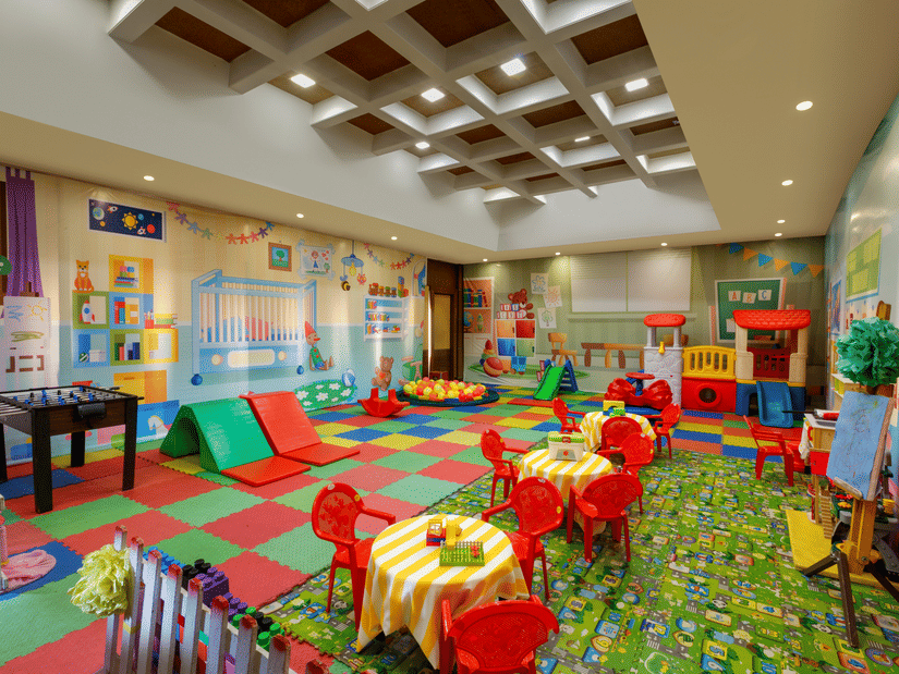 Children’s play area with small tables and chairs, colourful mats, toys, storage shelves, and ceiling lights at Heritage Village Resort & Spa, Manesar.