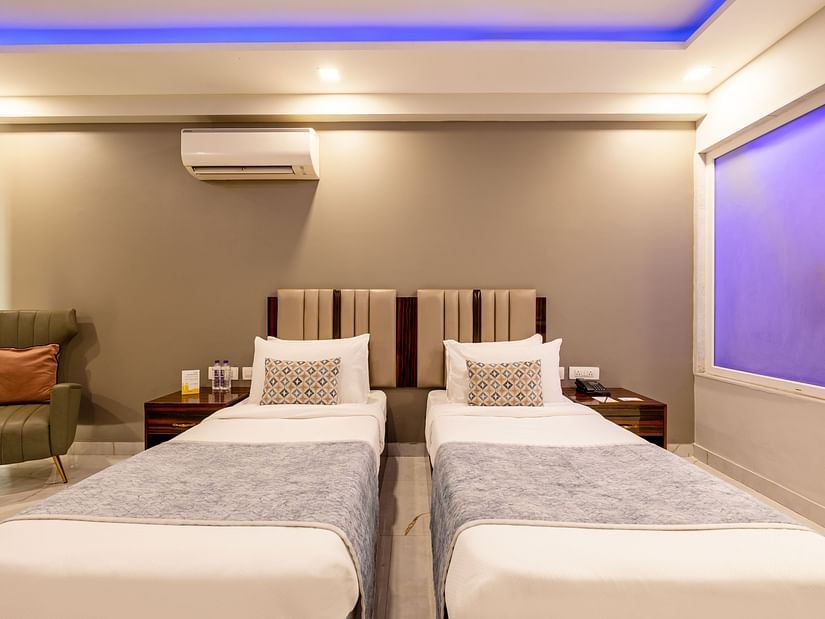 Twin beds in a room with soft lighting and a sofa chair at Hotel Bawa, Gurgaon.