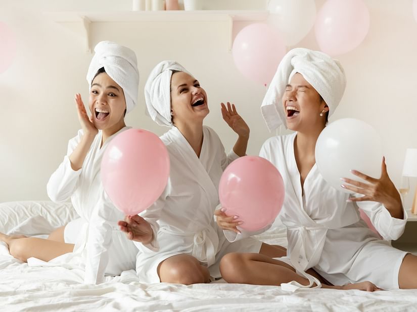 Image of three women laughing and having fun after a bath along with two pink balloons