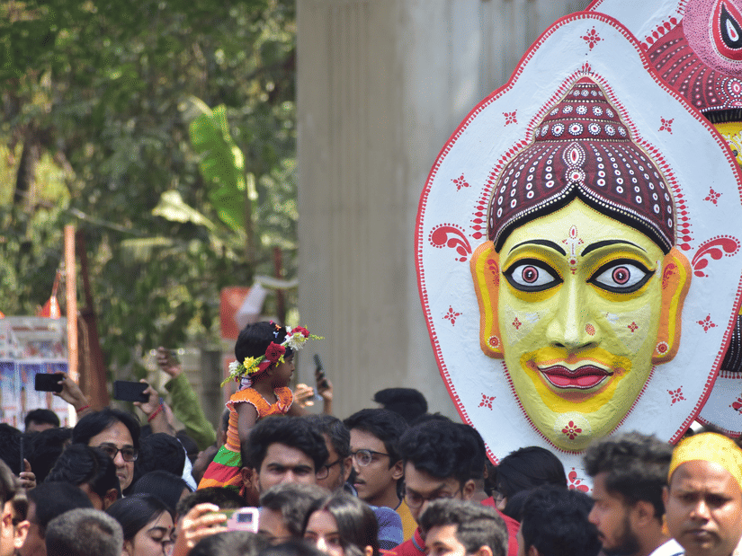 A procession on a road with many people carrying busts on a pole during the Bengali New Year in Kolkata