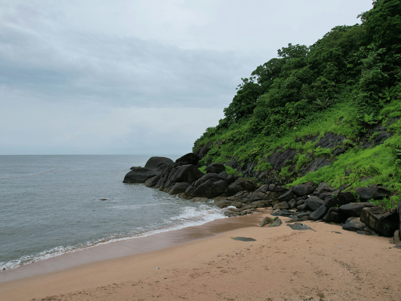 Shallow waves against the sandy shore under a clouded sky with a moss-covered mountain nearby