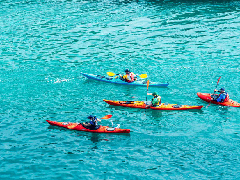 A group of four people kayaking in blue azure waters  as seen from above with waves on the waterbody seen.