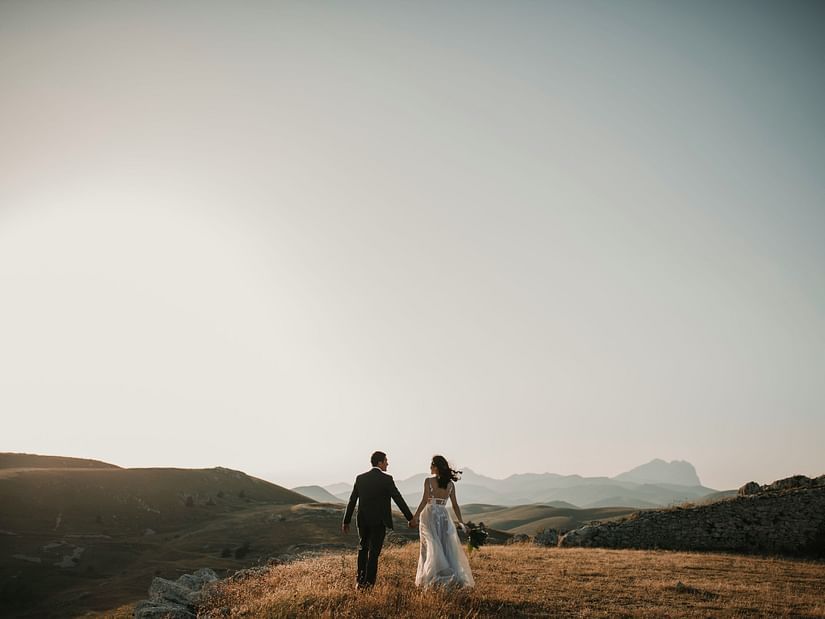 a wedding couple walking on a field during daytime
