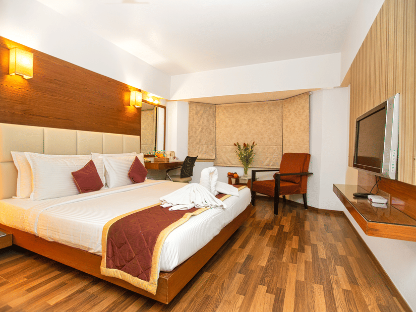 Spacious executive room with a king sized bed, wooden flooring, warm lighting, and modern amenities at Monarch Luxur Hotel, Bangalore.