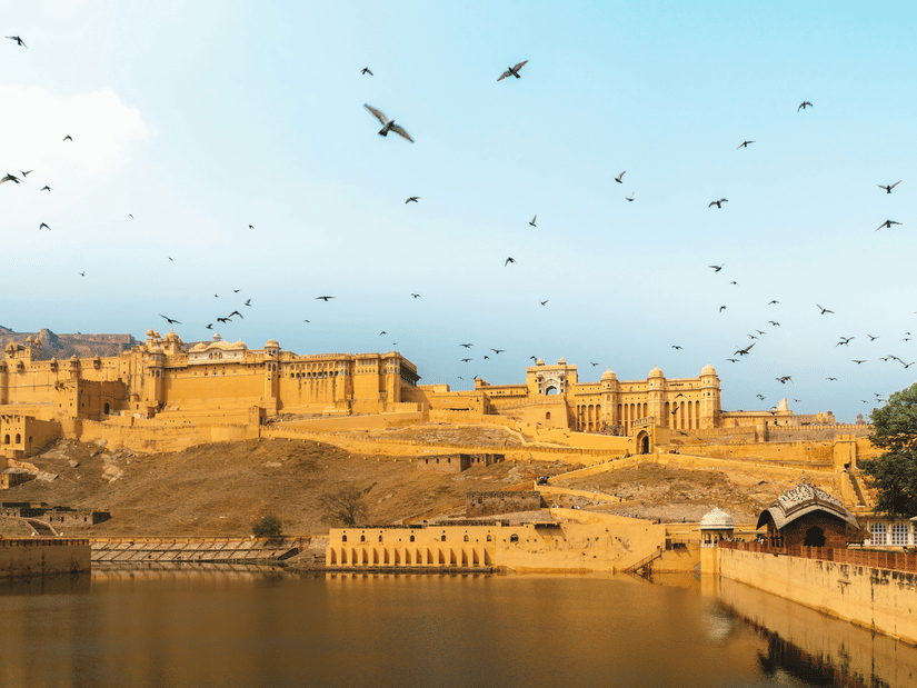 Facade of the Amber Fort under a clear sky with birds flying around on a sunny day