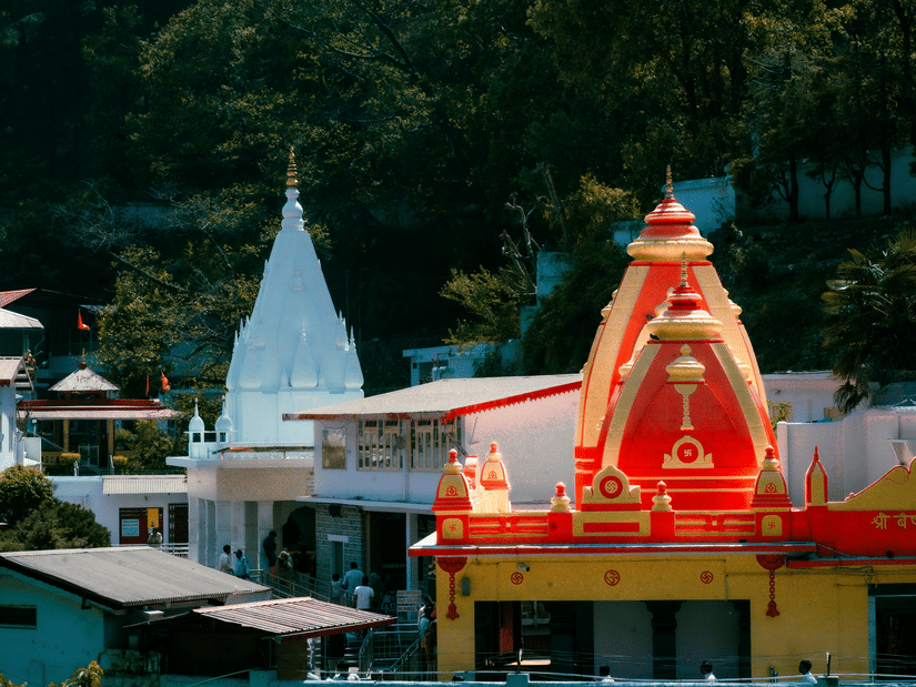A close up shot of the vibrant red and yellow dome of Kainchi Dham surrounded by white buildings and lush green trees.