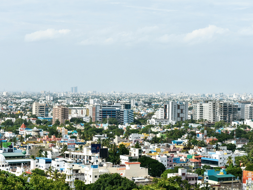 Panoramic view of a sprawling city centre with modern high-rise buildings and green trees under a bright, clear sky.